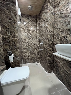 Ein modernes Badezimmer mit Marmorwand, Dusche, Toilette und Waschbecken.