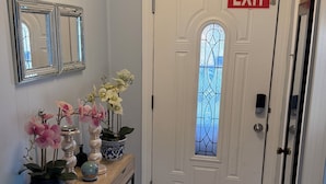 Un couloir avec une porte blanche portant l’inscription « SORTIE », une console ornée d’objets décoratifs et un miroir accroché au mur.