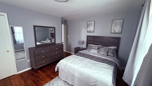 Une chambre à coucher avec un grand lit, une commode, une table de chevet, un miroir et deux cadres photo fixés au mur.