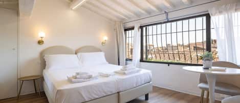Quarto com cama, mesas de cabeceira, janela com cortinas e vista para o exterior.