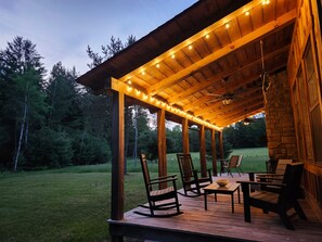 An outdoor wooden deck with chairs and tables, surrounded by a grassy area and trees. - Perfect Modern & Cozy 4-bedroom cabin with AC in Lake City; Outdoor Fireplace (Lake City)
