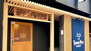 A wooden entrance with a traditional Japanese design, a blue sign for Tsukushi Hotel Kayabacho, and a modern building in the background. - KAYABACHO TSUKUSHI HOTEL (Tokyo)