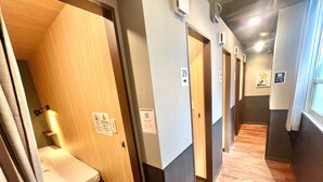 A hotel corridor with wooden flooring, numbered doors, and a bed with a curtain. - KAYABACHO TSUKUSHI HOTEL (Tokyo)