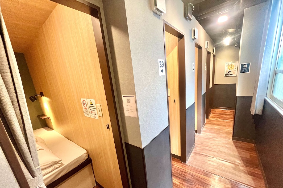 Pasillo de hotel con suelo de madera, puertas numeradas y una cama con cortina.