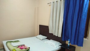 A neatly made bed with a white sheet and a folded blanket with a floral pattern. There is a wooden headboard and a small bedside table with a lamp.