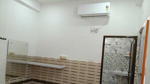 A bathroom with a shower, a red bucket, and a wall-mounted air conditioner.