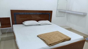 A neatly made bed with a wooden headboard, white bedding, and a folded beige towel on the footboard.