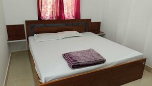 A single bed with a wooden frame and white bedding, a striped blanket on the bed, and a window with pink curtains.