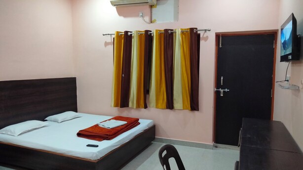 A bedroom with a bed, an air conditioner, curtains, a TV, and a door.