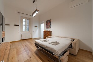 Ein Schlafzimmer mit Bett, Holzboden, Heizkörper, Fenster und einem an der Wand befestigten Kunstwerk.