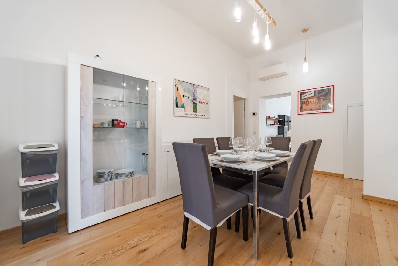 A dining area with a table set for four, a glass cabinet with dishes, and a wall with two framed pictures.