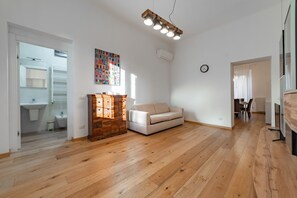 Ein geräumiger Wohnbereich mit Holzboden, einem weißen Sofa, einem Holzschrank und einem farbenfrohen Wandbild.
