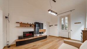 Una sala de estar moderna con televisor de pantalla plana, piso de madera, un sofá y una ventana con persianas.