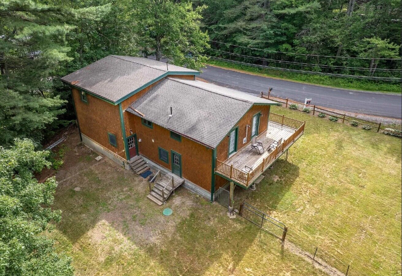 A two-story building with a porch, a small staircase, and a fenced yard.