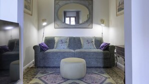 Ein Wohnzimmer mit grauem Sofa, einem runden Ottomanen, einem großen Spiegel und einem Teppich mit Muster.