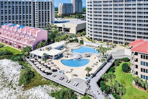 Ein Resort mit mehreren Schwimmbecken, einem Strandbereich und verschiedenen Gebäuden, darunter ein Hotel mit rotem Dach.