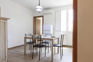 A dining area with a wooden table and chairs, an air conditioning unit, and a window with blinds. - Serragli Deluxe Apartament (Firenze)