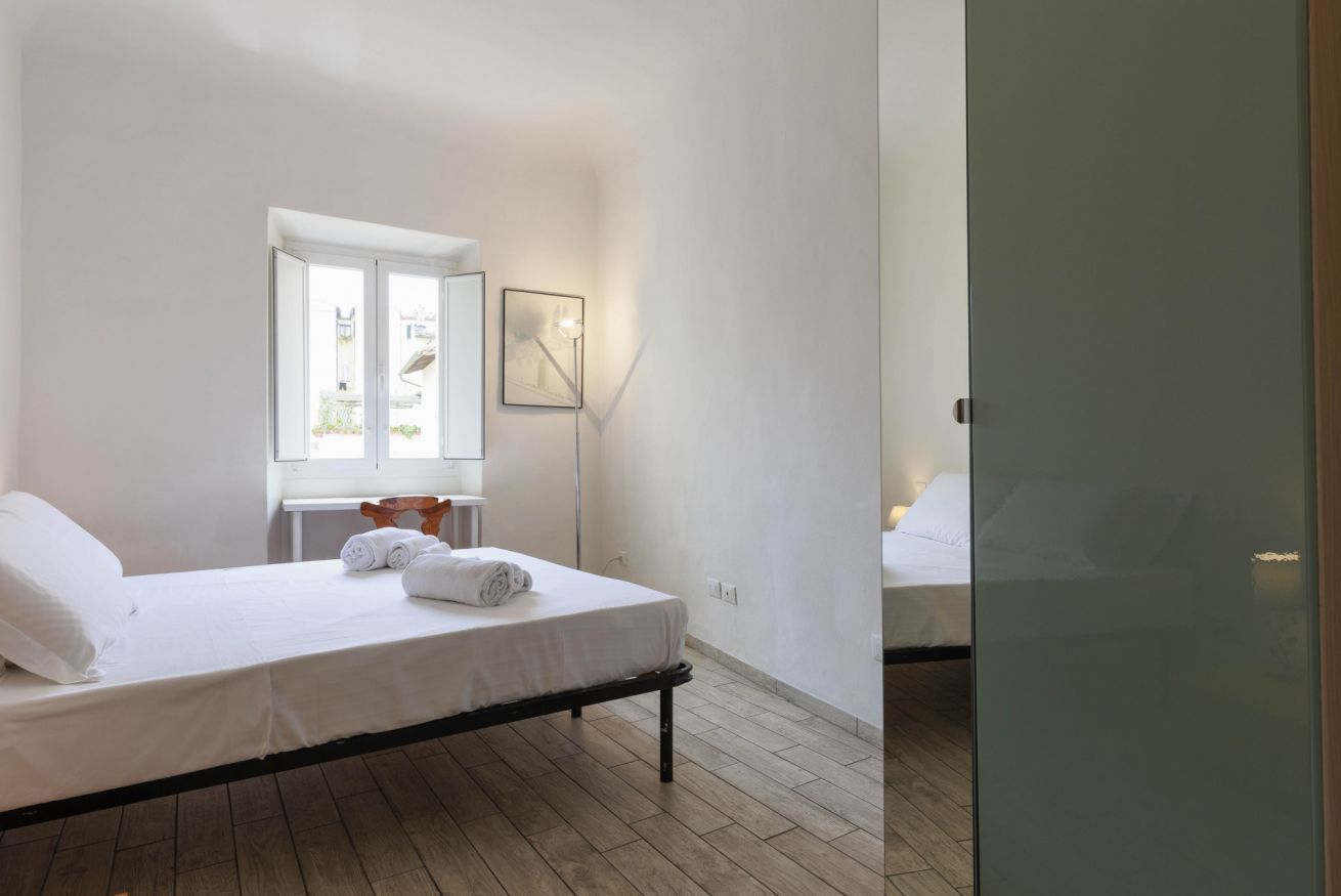 A bedroom with a single bed, a window, and a bedside table with a lamp.