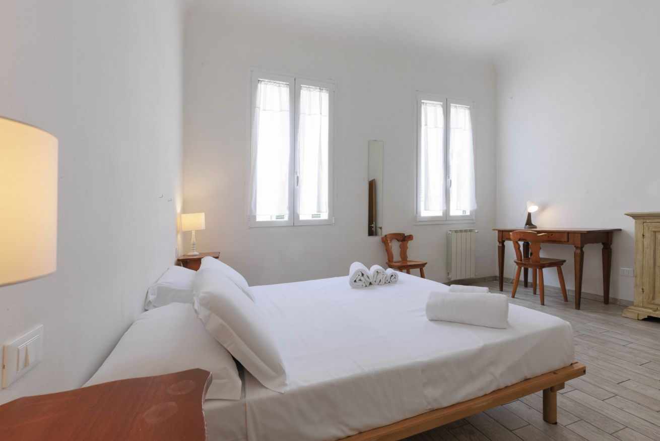 Une chambre à coucher avec un lit, un bureau, une chaise et deux fenêtres.
