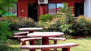 A building with a red brick exterior, a large air conditioning unit mounted on the wall, and a garden with multiple round stone tables. - Hotel Green Crystal (Mahabaleshwar)