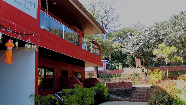 A two-story building with a red facade, a balcony with railings, and a stone wall with steps leading up to it. - Hotel Green Crystal (Mahabaleshwar)