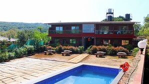 A hotel with a swimming pool, outdoor seating, and a view of the hills. - Hotel Green Crystal (Mahabaleshwar)