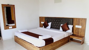 A large wooden bed with a headboard, two nightstands, and a mirror on the wall. - Hotel Green Crystal (Mahabaleshwar)