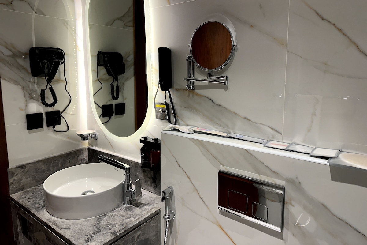 A bathroom with a marble sink, a large mirror, a hairdryer, and a towel rack.