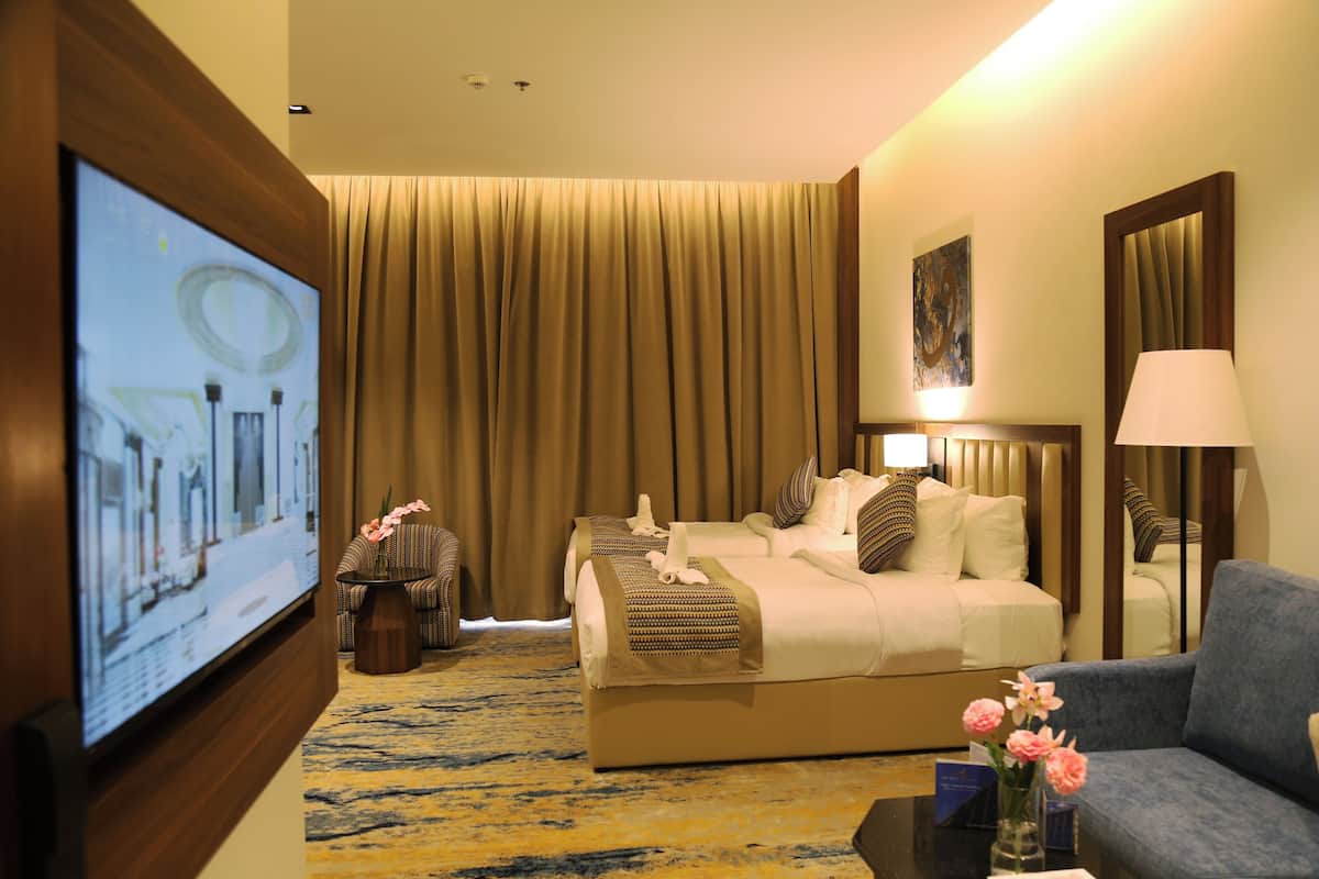 Una habitación de hotel con una cama grande, televisión, sofá, mesa de centro y un florero con flores.
