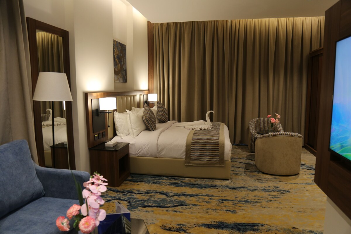A hotel room with a bed, a sofa, a chair, a TV, and a carpeted floor.