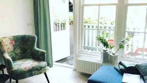 Un salon avec un fauteuil à motifs floraux, un canapé bleu et un tapis à motifs. On aperçoit une fenêtre donnant sur l’extérieur, ainsi qu’un radiateur.