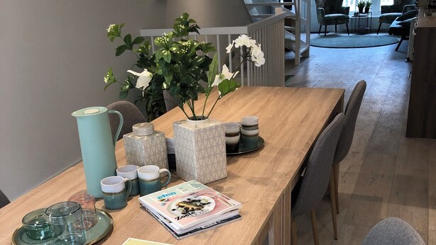 Une table de salle à manger en bois, avec un magazine, un vase de fleurs et divers objets en verre.
