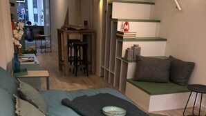 Une chambre à coucher avec un lit, une petite table sur laquelle se trouve un bol, une chaise et une bibliothèque remplie de livres et ornée d’une lanterne.