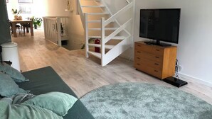 Un salon moderne avec un escalier, un téléviseur et un coin repas à l’arrière-plan.