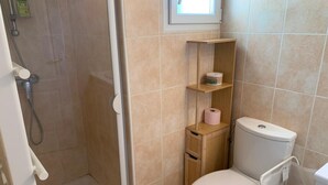 Un baño pequeño con inodoro, ducha y estante con artículos de aseo.