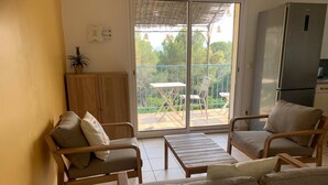 Una sala acogedora con muebles de madera, una puerta corrediza de cristal a un balcón y un refrigerador.
