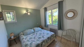 Un dormitorio con cama, una silla, una ventana, un radiador y un espejo fijado a la pared.