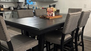 A dining area with a dark wooden table and four upholstered chairs, a kitchen in the background, and a 'let's eat' sign above the table. - Updated - 3-bedroom house in delightful Sevierville, hot tub, dog friendly (Sevierville)