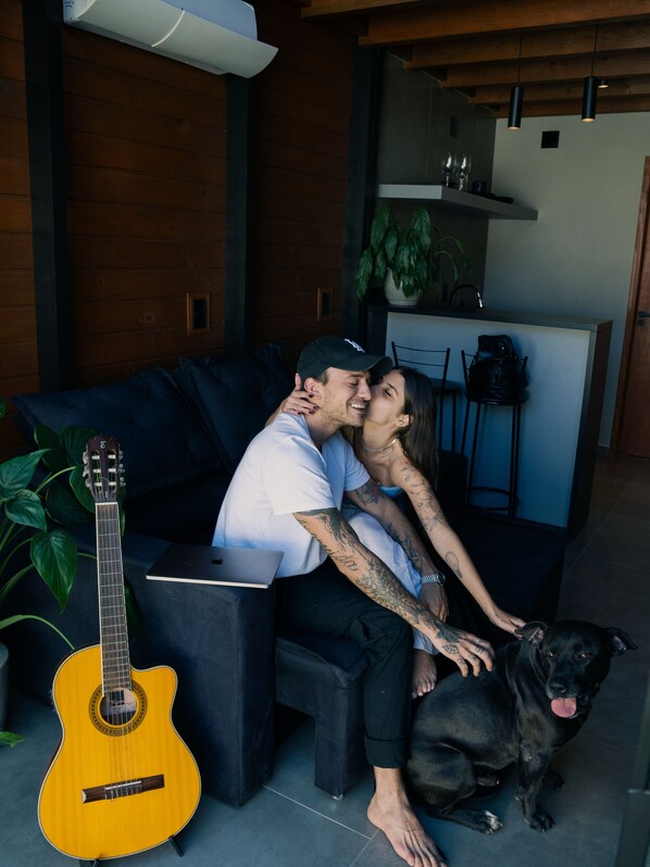 A couple sitting on a dark blue sofa with a guitar and a dog beside them.