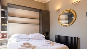 A modern hotel room with a large bed, a built-in wardrobe, a round mirror, and a radiator. - Ponte Vecchio Terrace Suite with Jacuzzi (Florence)