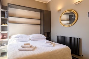 A modern hotel room with a large bed, a built-in wardrobe, a round mirror, and a radiator. - Ponte Vecchio Terrace Suite with Jacuzzi (Florence)