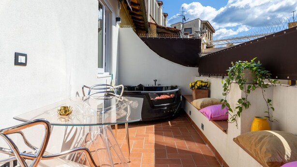 A modern outdoor patio with a glass table and chairs, a black outdoor heater, and a small seating area with cushions. - Ponte Vecchio Terrace Suite with Jacuzzi (Florence)