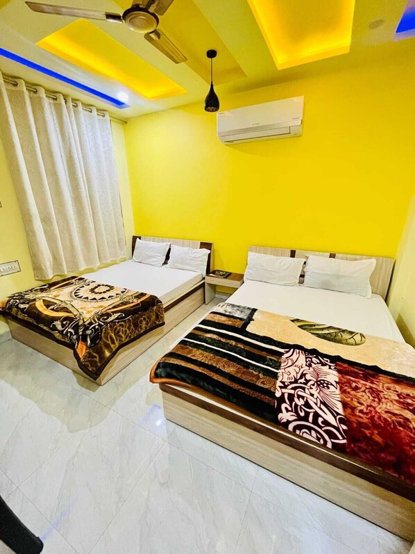 A hotel room with two beds, a ceiling fan, an air conditioning unit, and a window with curtains. - Hotel Shree Sanwariya (Sikar)