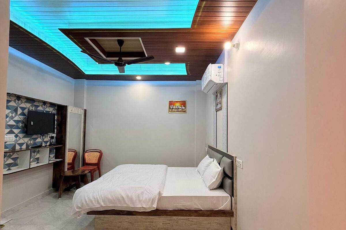 A bedroom with a bed, a ceiling fan, a TV, and a small table with chairs.