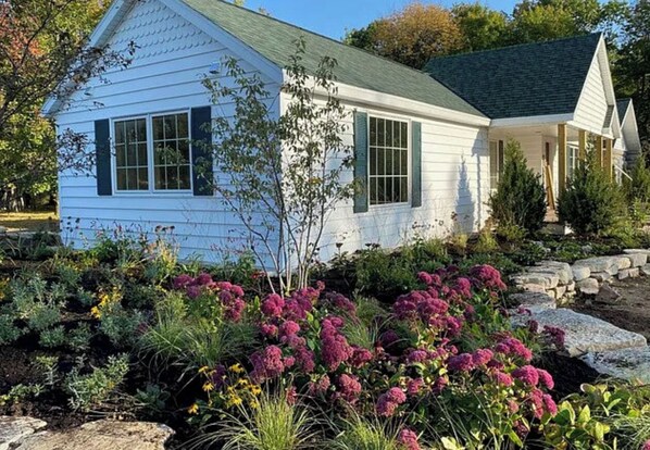 A white house with a green roof, surrounded by a garden with purple flowers and various plants. - Spacious getaway in peaceful Ephraim - just few minutes away from Sister Bay (Sister Bay)