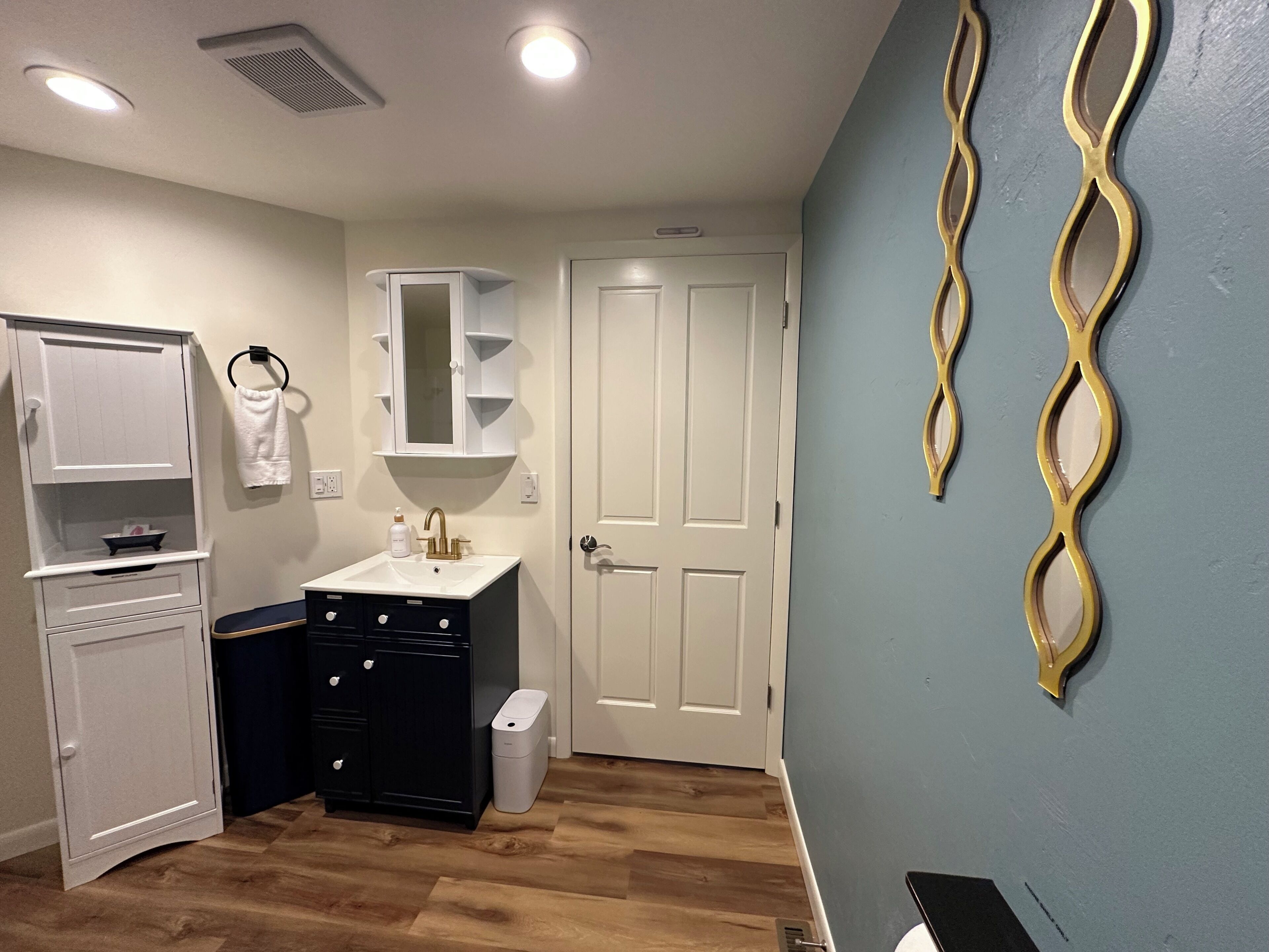 A bathroom with a white cabinet, a sink with a mirror, a towel rack, and a door.