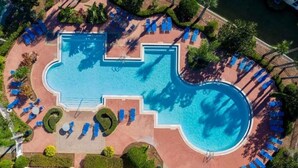 Vista aérea de una zona de piscina de hotel con una piscina grande central, tumbonas y follaje circundante.