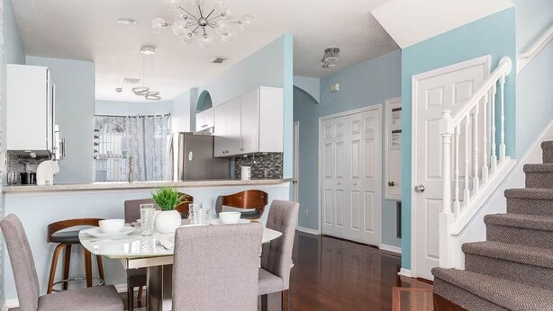 Una cocina moderna con armarios blancos, una campana extractora de acero inoxidable y un comedor con mesa blanca y sillas grises.