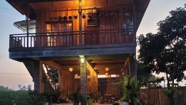 A two-story wooden house with a balcony, a staircase leading to the upper floor, and a garden area with plants and a pathway. - Bua Guest House (Medan)