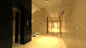 A modern hotel corridor with marble flooring, a glass elevator, and a sign indicating the hotel name. - Ozone Hill Resorts (Yercaud)